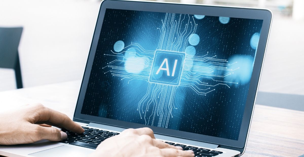 komputer na którym wyświetla się napis Al mówiący o sztucznej inteligencji, obok komputera widać dłonie